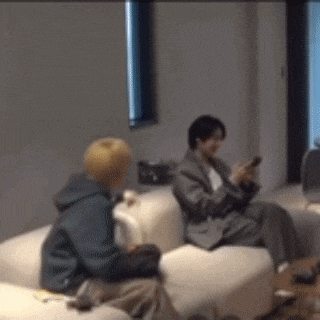 two people are sitting on a couch in a living room looking at their cell phones .