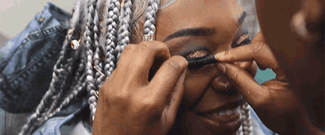 a woman with braids is getting her eye makeup applied by a man