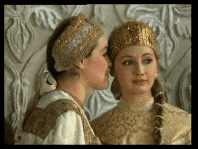 a woman whispering into another woman 's ear while wearing a crown