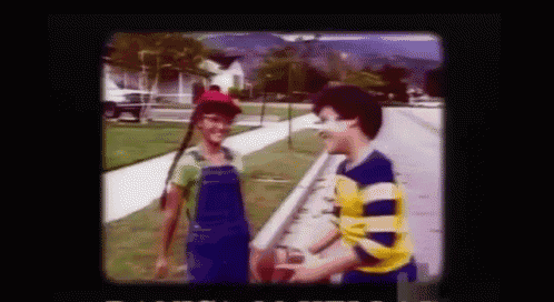 a boy and a girl are standing on a sidewalk talking to each other