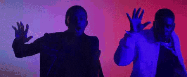 a couple of men are standing next to each other in a dark room with their hands up in the air .