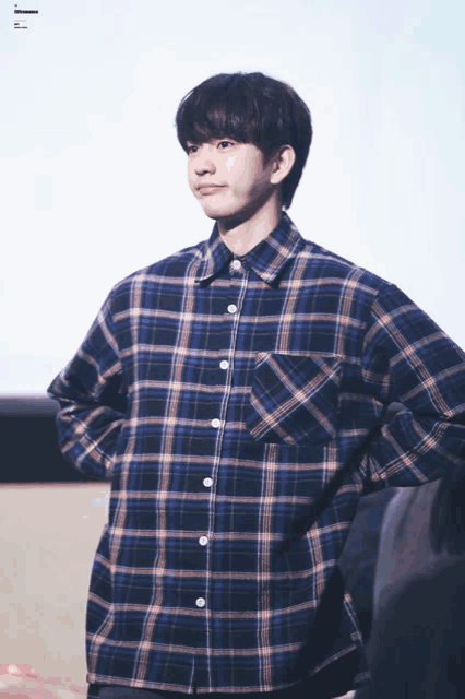 a young man wearing a plaid shirt is standing with his hands behind his back
