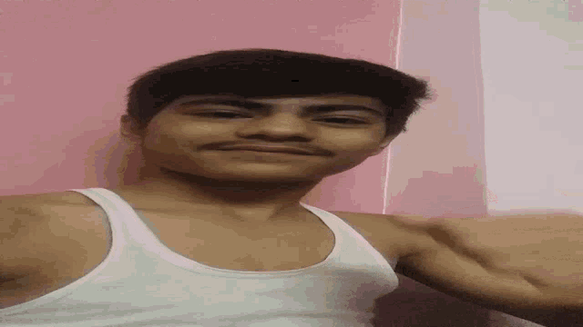 a young man in a white tank top is taking a selfie in front of a pink wall