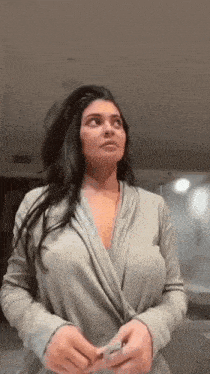 a woman in a gray robe is standing in front of a mirror .