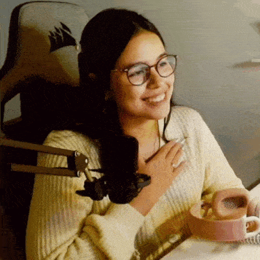 a woman wearing glasses is smiling in front of a microphone while holding a cup of coffee