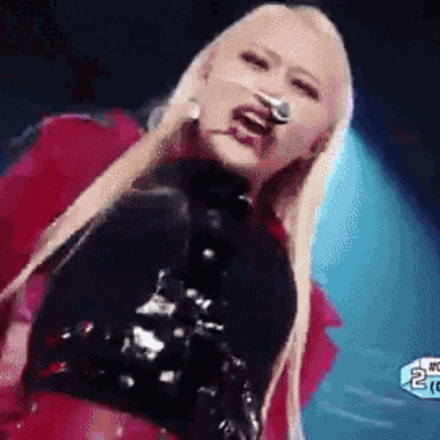a woman with blonde hair is singing into a microphone while wearing a red jacket and black top .