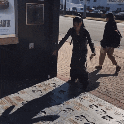 a woman walking down a sidewalk with a poster on the wall that says wayne james
