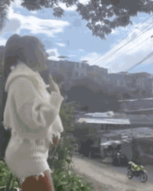 a woman in a white sweater stands in front of a motorcycle on a street