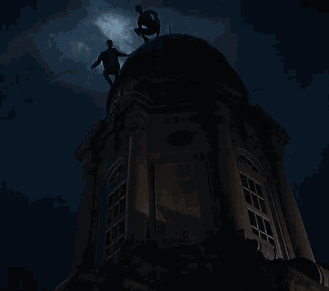 two men are standing on top of a very tall building at night