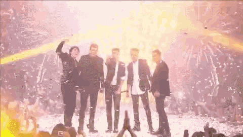 a group of men are standing on a stage in front of a crowd with confetti falling .