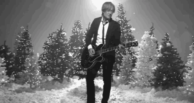 a man in a suit and tie plays a guitar in front of christmas trees