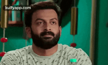 a man with a beard is sitting in front of a green wall and looking at the camera .