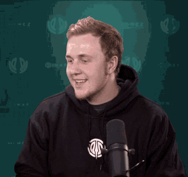 a man in a black hoodie stands in front of a microphone with the word hirez in the background
