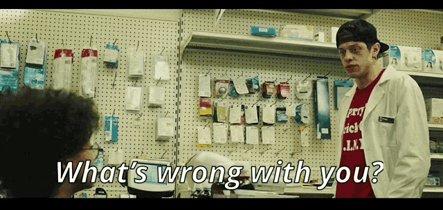 a man in a lab coat is talking to another man in a red shirt that says ' what 's wrong with you '