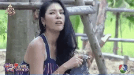 a woman in a blue tank top is standing in front of a wooden fence .