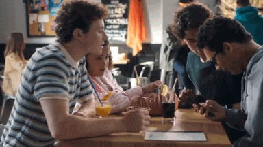 a group of people are sitting at a table looking at their cell phones