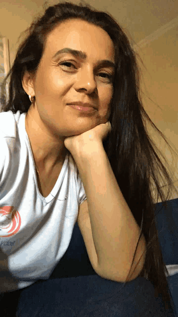 a woman with long dark hair wearing a white shirt with a pink circle on it