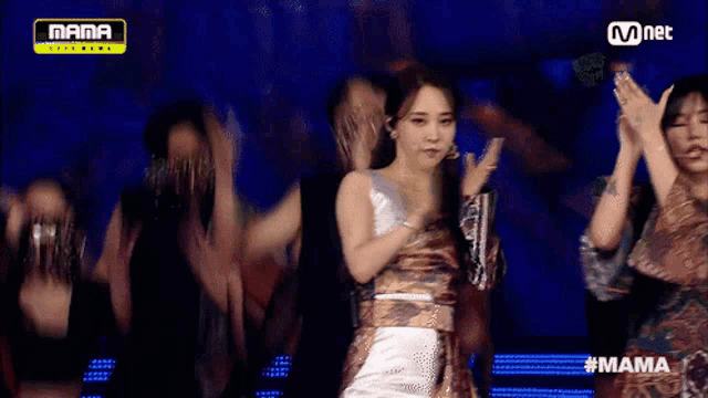 a woman in a white dress is standing in front of a group of dancers on a stage ..