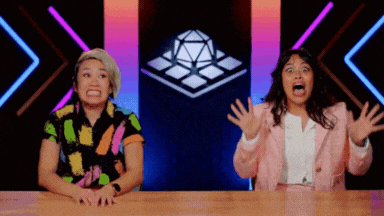 two women are sitting at a table with their arms outstretched in front of a cube .
