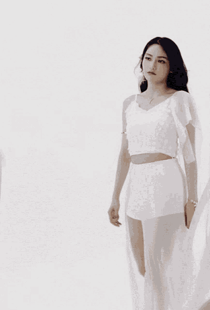 a woman in a white crop top and shorts stands in front of a white wall
