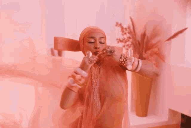 a woman in a pink dress and head scarf is holding a glass