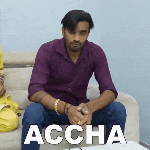 a man in a purple shirt is sitting on a couch with the word accha written in white