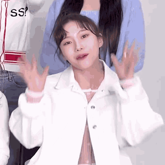 a girl in a white jacket is making a funny face with her hands up .