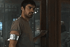 a man with a bandage on his arm is standing in front of a window .