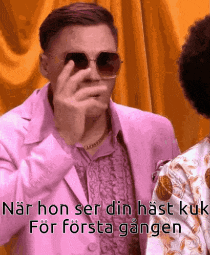 a man in a pink suit and sunglasses is covering his eyes with his hand