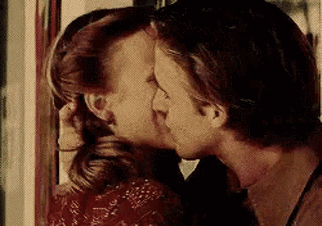 a man and a woman are kissing in front of a mirror .