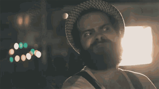 a man with a beard wearing a hat looks up at something