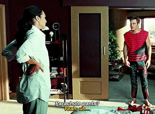 a man and a woman are standing in a room and the man is asking the woman if she has parachute pants