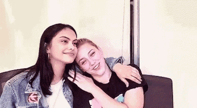 two young women are sitting next to each other on a couch and hugging each other .