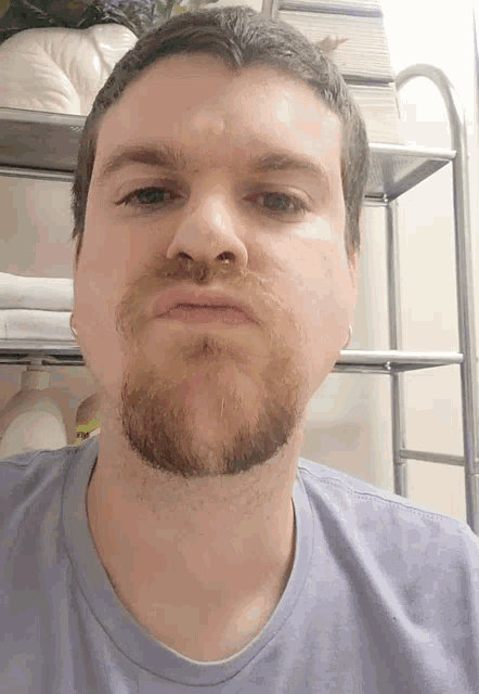a man with a beard wearing a purple shirt is making a funny face