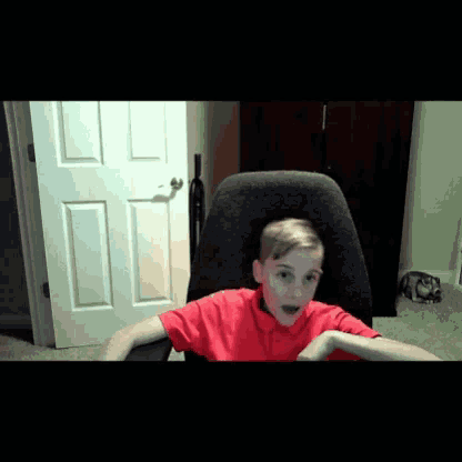 a young boy in a red shirt sitting in a chair