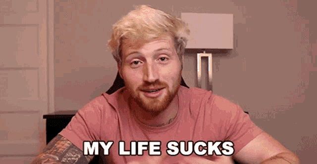 a man with a beard is sitting in a chair and says my life sucks