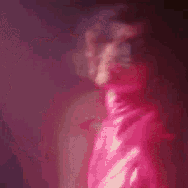 a woman in a pink turtleneck is standing in front of a bear with her hair blowing in the wind .