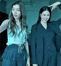 two women are standing next to each other and one is wearing a suit and smiling .