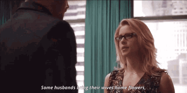 a woman with glasses is talking to a man and says some husbands bring their wives home flowers