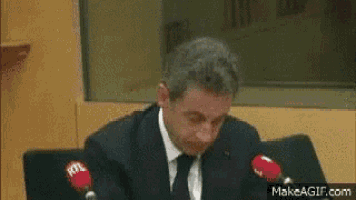 a man in a suit and tie is sitting at a table with two microphones .