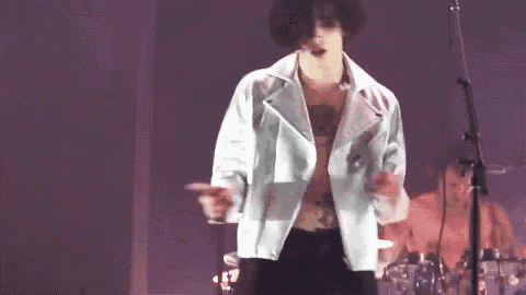 a man without a shirt is standing on a stage with a microphone .