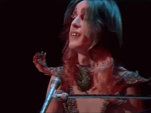 a woman is singing into a microphone while wearing a snake around her neck .