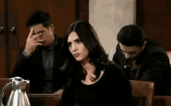 a man is smoking a cigarette while a woman sits at a table in a courtroom .