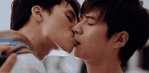 two young men are kissing each other with their eyes closed .