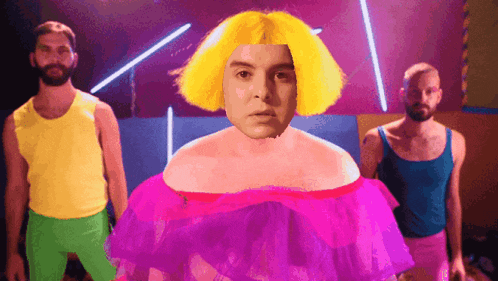 a man with a yellow wig and a pink dress is surrounded by two other men