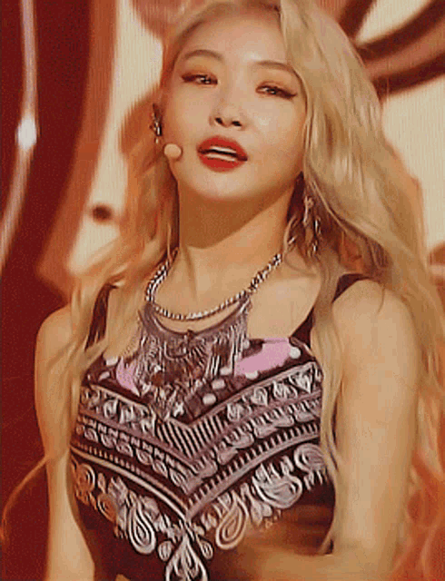 a woman with blonde hair is wearing a necklace and a top with a pattern on it