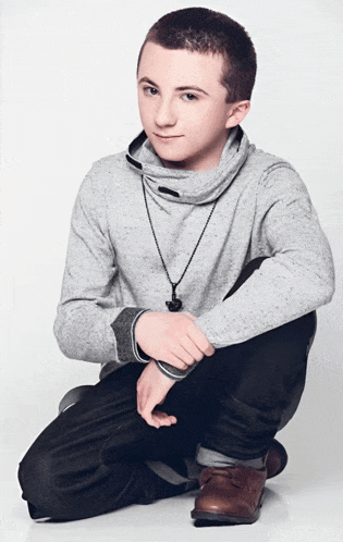 a young boy wearing a grey sweater and a black necklace