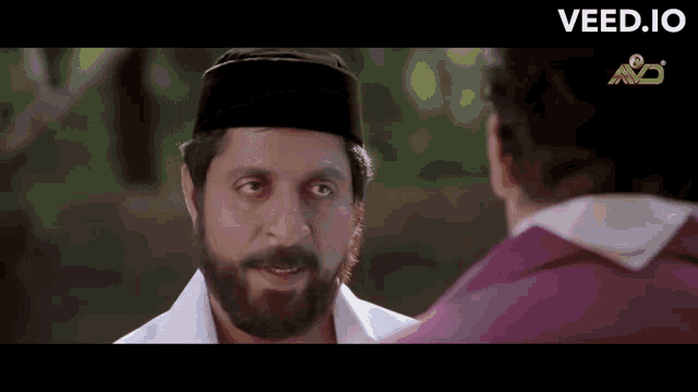 a man with a beard is wearing a black hat and talking to another man ..