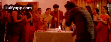 a man is cutting a birthday cake in front of a crowd of people .