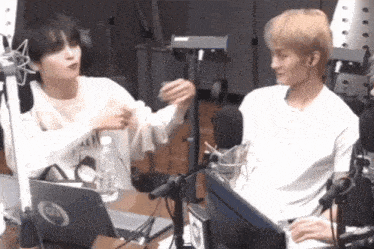 two men are sitting in front of a microphone and a laptop